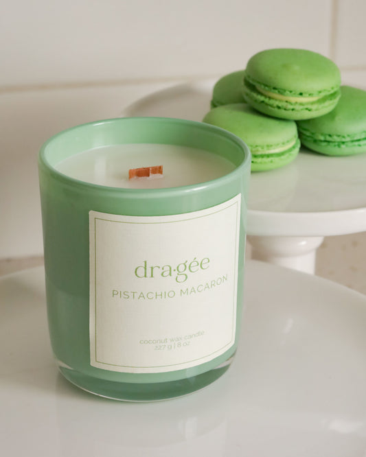 Green glass candle with green macarons around on cake platers in a kitchen setting.