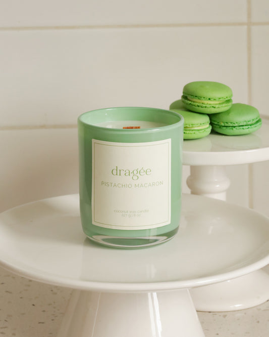 Green glass candle with green macarons around on cake platers in a kitchen setting.
